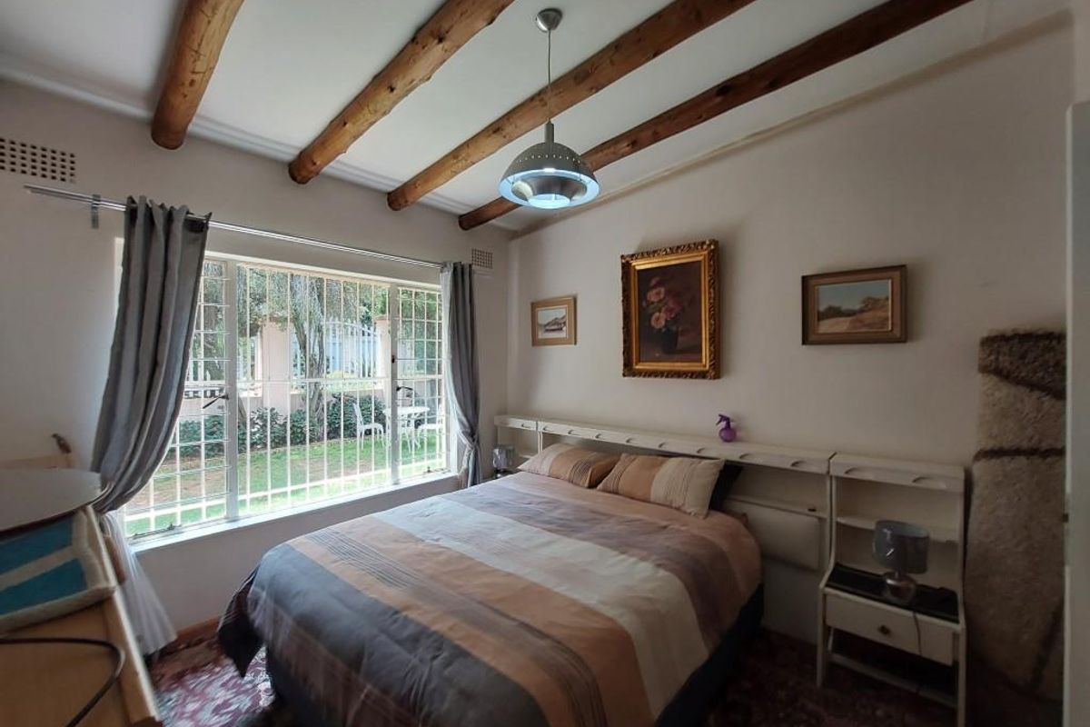 A bedroom featuring exposed timber ceiling beams, a large window with security bars, and built-in headboard shelving.