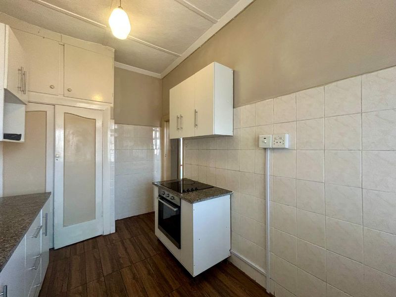 A functional kitchen featuring built-in cabinetry, an electric hob, oven, and tiled splashbacks, presenting a clean and ready-to-update space.