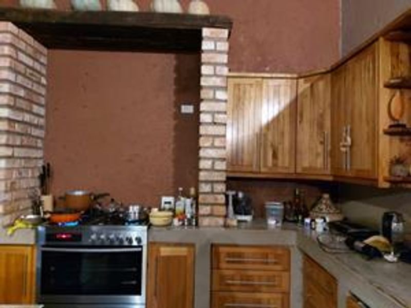 Rustic kitchen featuring wooden cabinetry, concrete countertops, and a distinctive brick-framed cooking area with a built-in oven and gas hob.