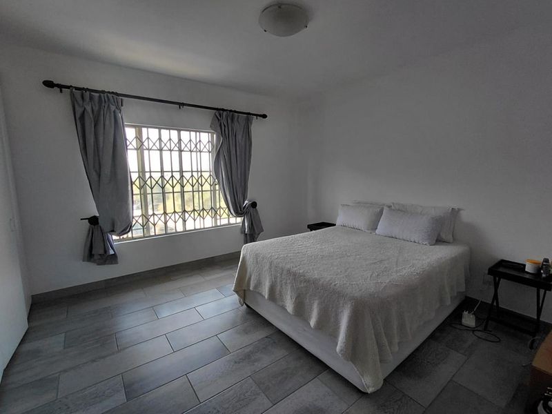 A bedroom featuring tiled flooring, a window with a security gate, and a ceiling light fixture.