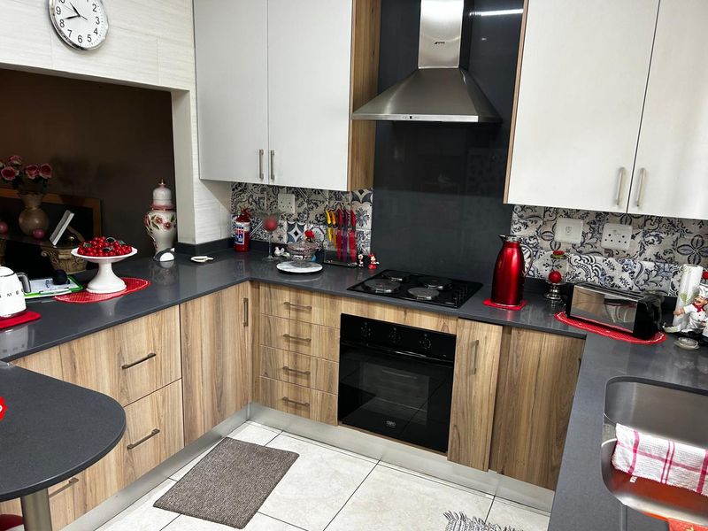 Modern kitchen featuring wood-grain cabinetry, dark stone countertops, a built-in oven, electric hob, and stainless steel extractor fan with decorative tiled splashback.