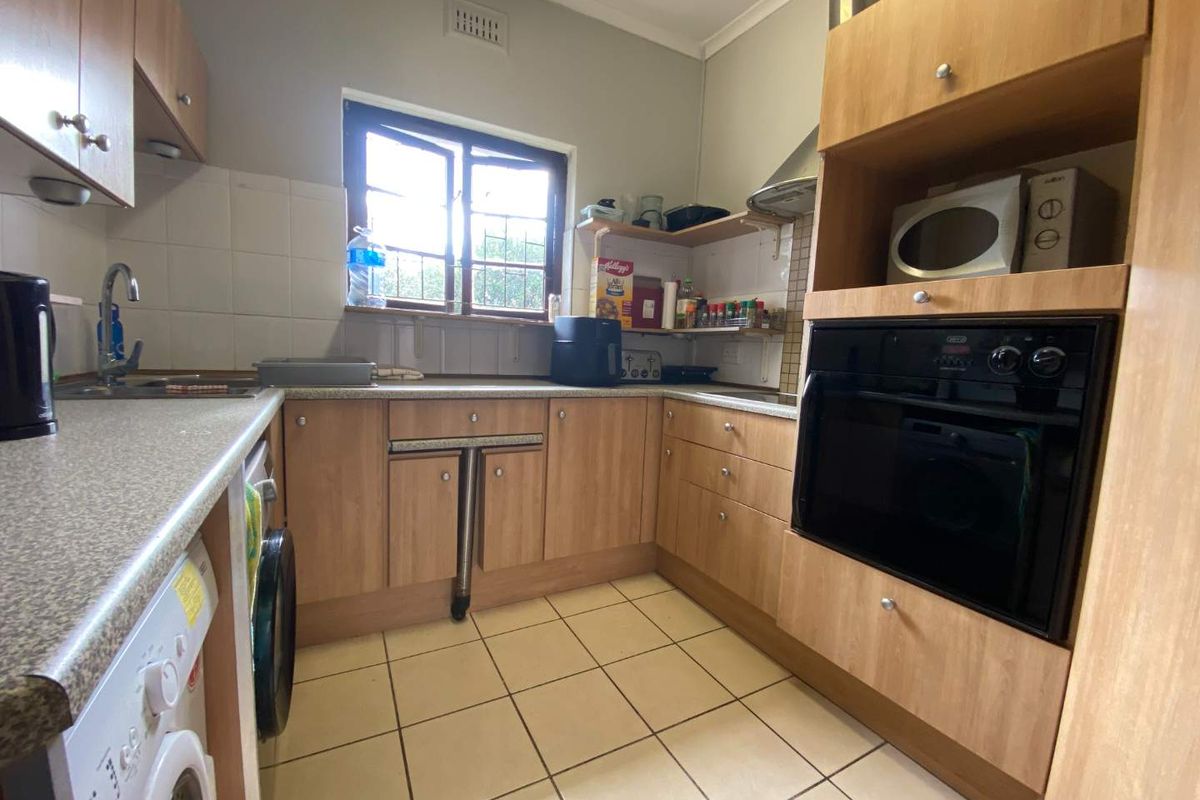 A functional kitchen featuring laminate cabinetry, built-in oven, extractor fan, tiled backsplash, and tiled flooring with a window for natural light.