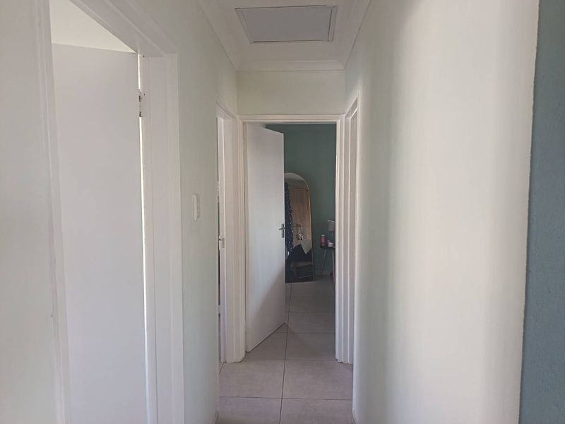A clean, neutral hallway featuring tiled flooring and a ceiling access hatch, providing access to multiple rooms within the home.
