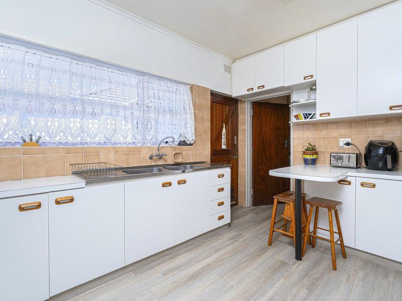 A functional kitchen featuring white laminate cabinetry, a double bowl stainless steel sink, tiled splashback, and a convenient built-in breakfast bar.