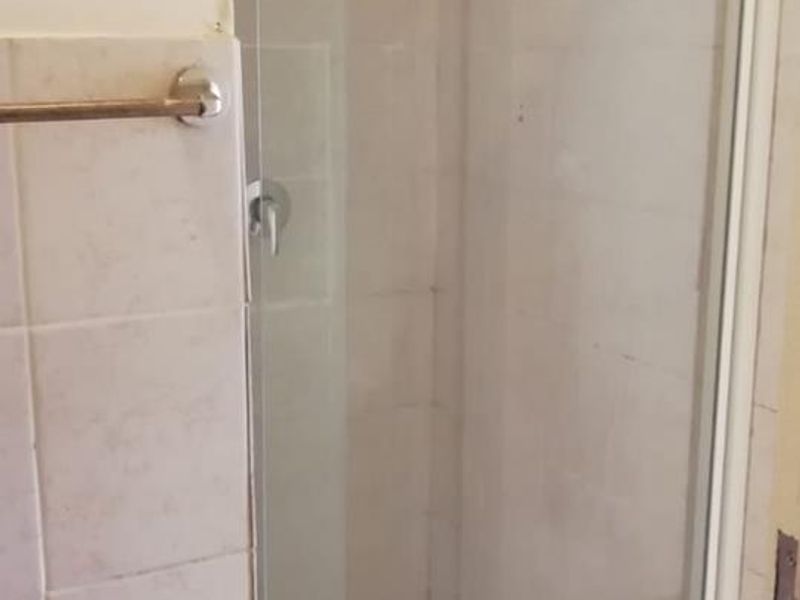 A compact shower stall featuring a glass door, tiled walls, and floor, requiring minor maintenance to refresh the grout and tile surfaces.