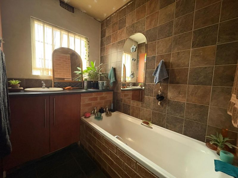 A dated bathroom featuring a built-in vanity with a drop-in basin, a bathtub, and dark brown wall tiling.