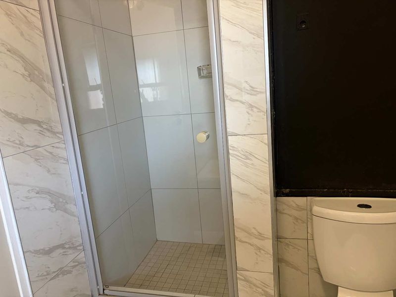 A bathroom featuring a glass-enclosed shower with marble-look wall tiles and a standard toilet, requiring minor cosmetic updates to the wall finish.