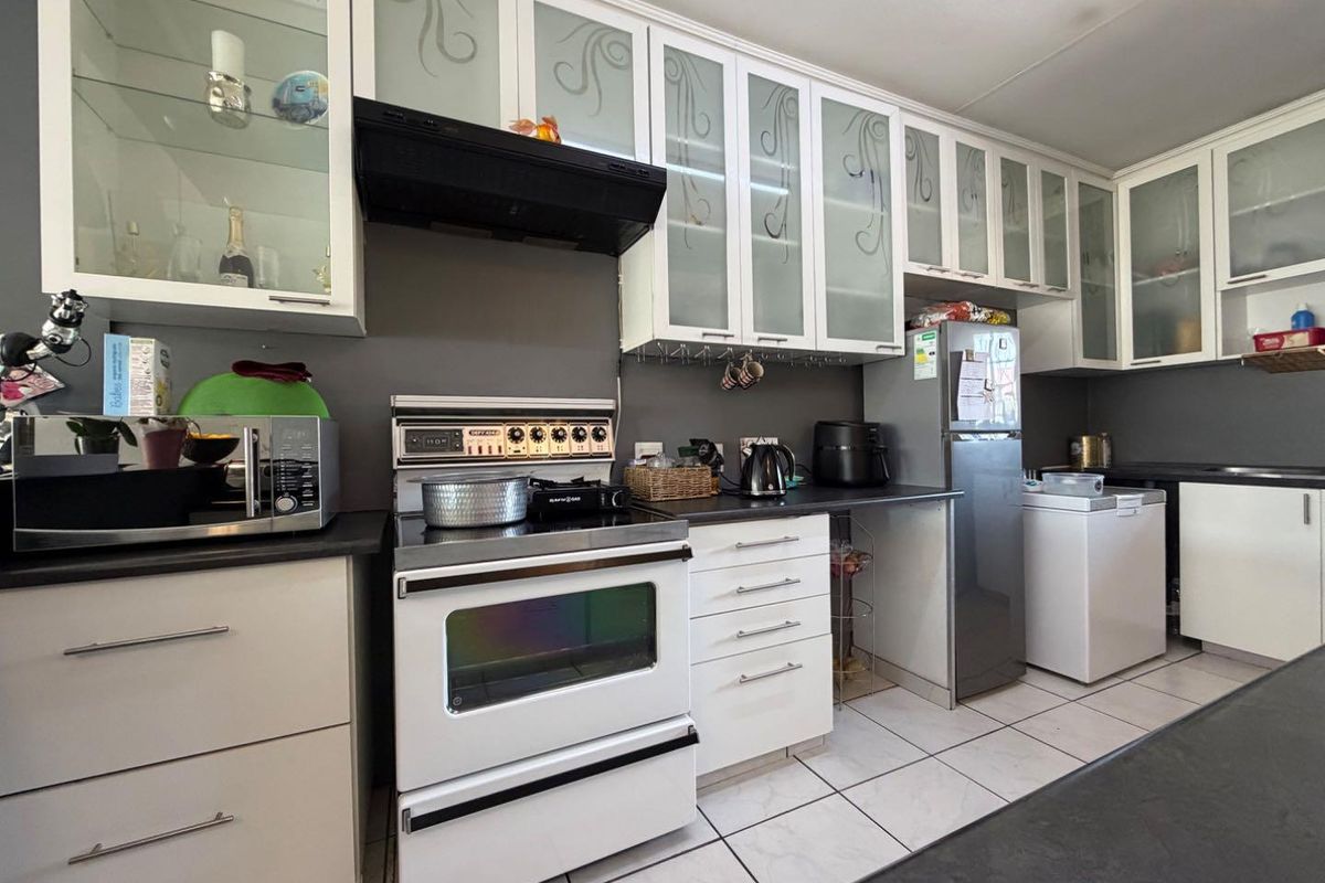 A functional kitchen featuring white cabinetry with glass inserts, dark countertops, tiled flooring, and a built-in extractor fan above the stove.