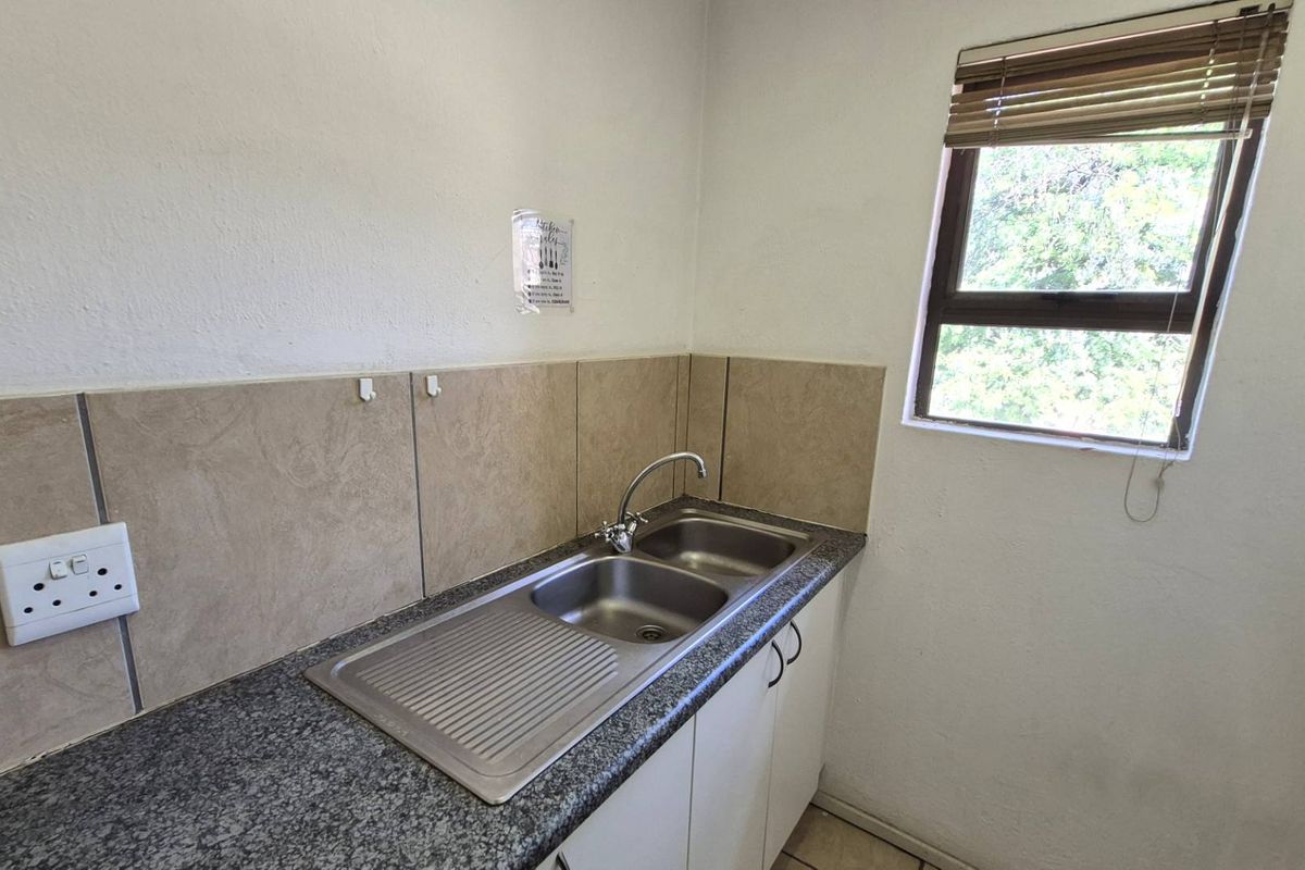 A functional kitchenette area featuring a double stainless steel sink, granite-look countertop, tiled backsplash, and built-in base cabinetry.