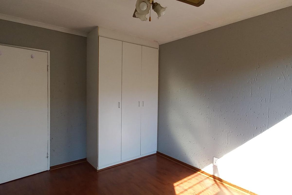 An empty bedroom featuring laminate flooring, grey textured walls, and a built-in white wardrobe.