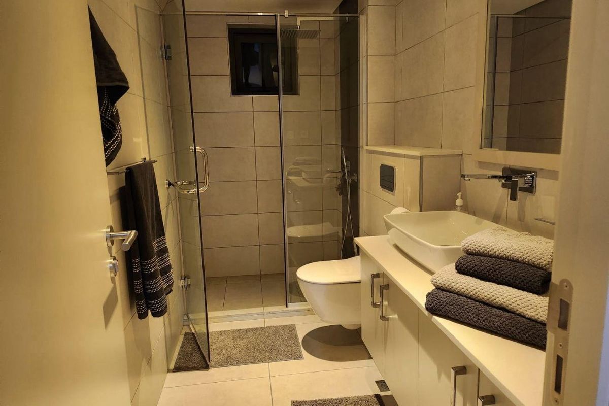 Modern bathroom featuring a wall-mounted toilet, glass-enclosed walk-in shower, and a vanity with a vessel sink.