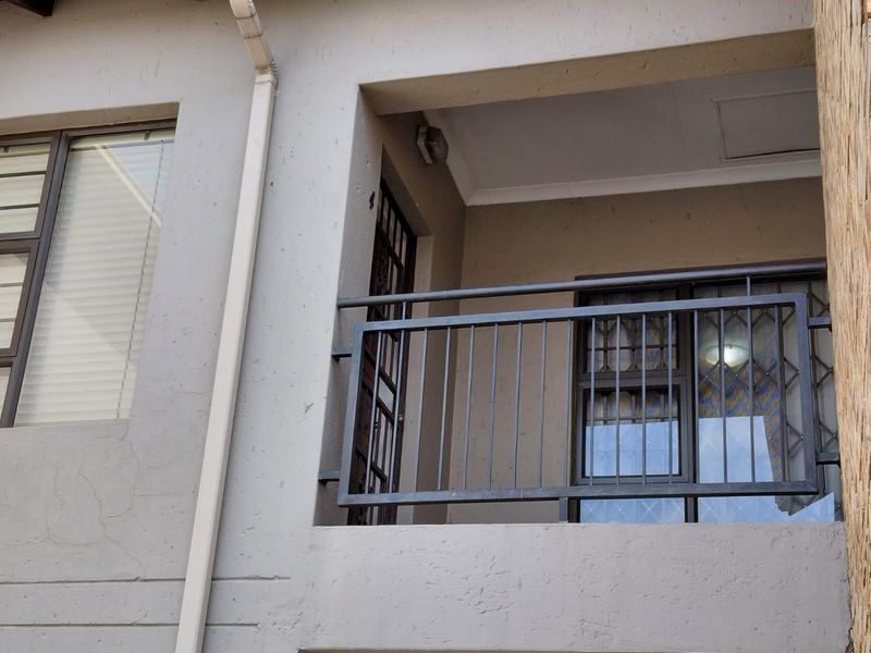 A covered balcony featuring a metal balustrade, aluminium window frames, and a security gate, showing minor exterior plaster cracking.
