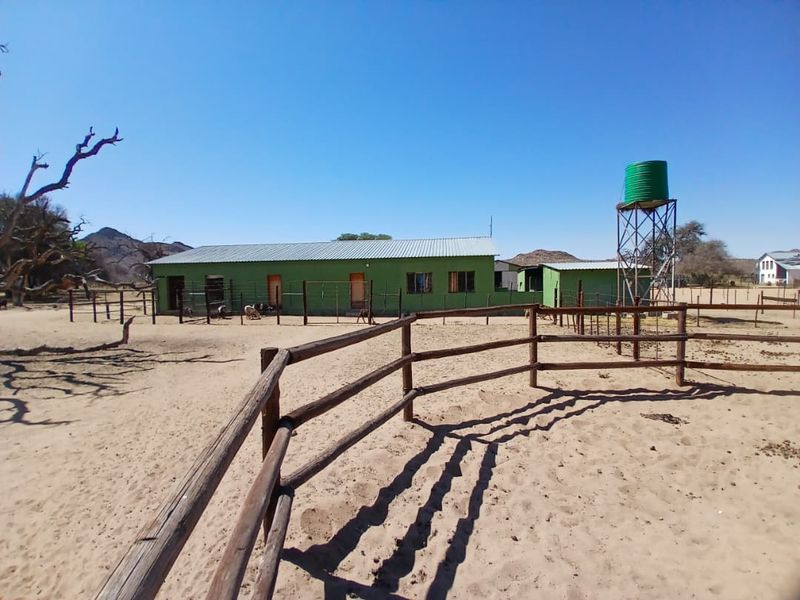 Exterior view of a small holding featuring a long outbuilding with a corrugated metal roof, water storage tank, and extensive timber fencing.