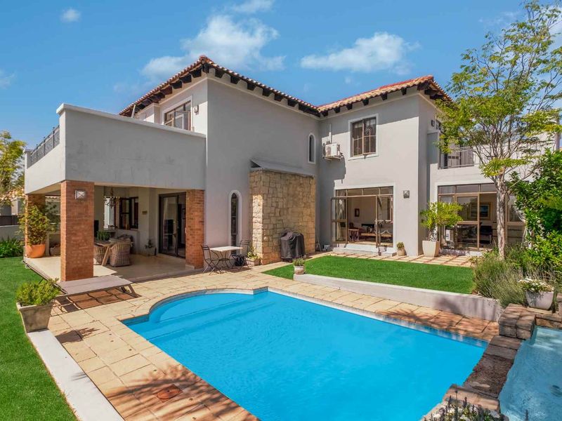 Rear view of a two-story residence featuring a swimming pool, covered patio area, landscaped garden, and a mix of stone and rendered exterior finishes.