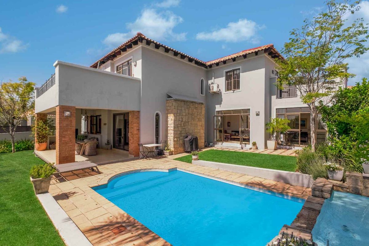 Rear view of a two-story residence featuring a swimming pool, covered patio area, landscaped garden, and a mix of stone and rendered exterior finishes.