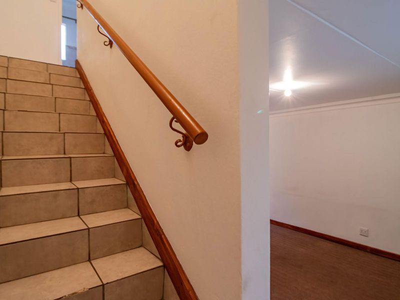 A functional hallway featuring a tiled staircase with a wooden handrail, leading to an adjacent open living space with neutral finishes.