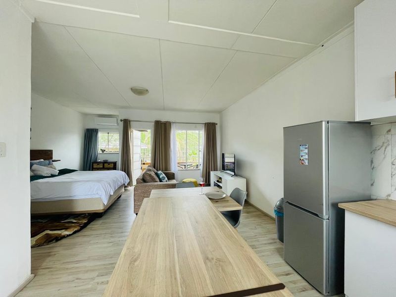 Open-plan studio apartment featuring a combined living, sleeping, and kitchen area with light wood-look flooring and modern cabinetry.