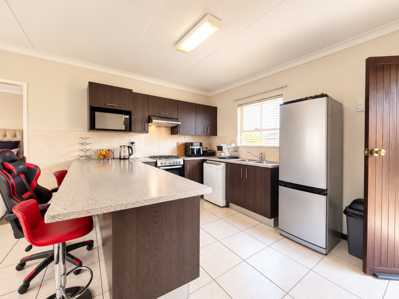 Functional kitchen featuring dark wood cabinetry, stone-look countertops, built-in oven with gas hob, and tiled flooring, offering a practical layout for daily use.