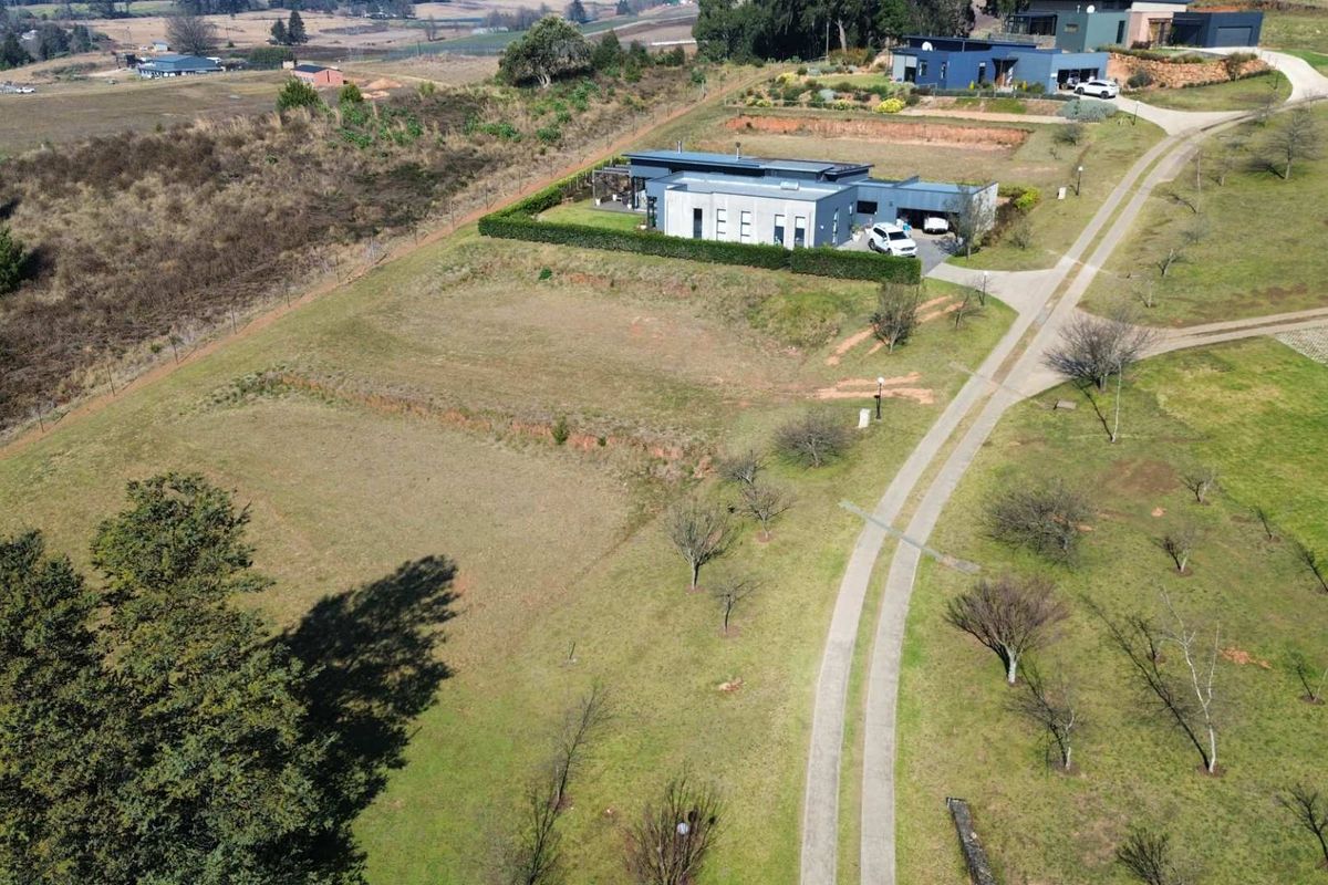 Aerial view of a residential vacant land plot featuring a paved driveway and established landscaping within a rural estate setting.