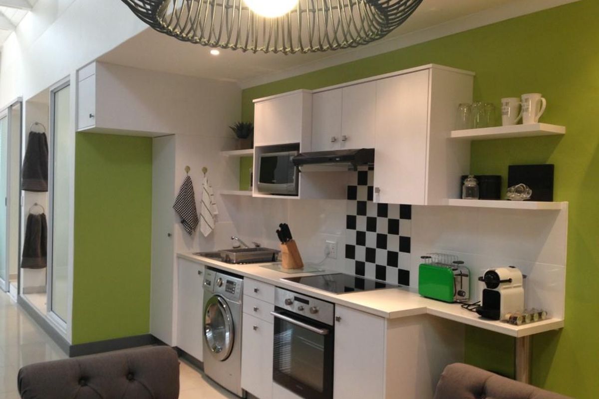 Compact kitchen featuring white cabinetry, integrated oven, hob, extractor fan, built-in microwave, and a laundry connection, set against a vibrant green feature wall.