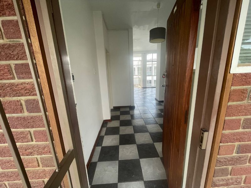 Entrance hallway featuring checkered tile flooring, a timber door, and a security gate, leading into an open-plan living area.