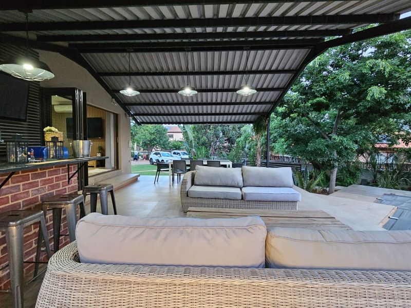 Spacious covered patio featuring a built-in brick bar with granite countertop, pendant lighting, and seamless access to the garden through sliding glass doors.