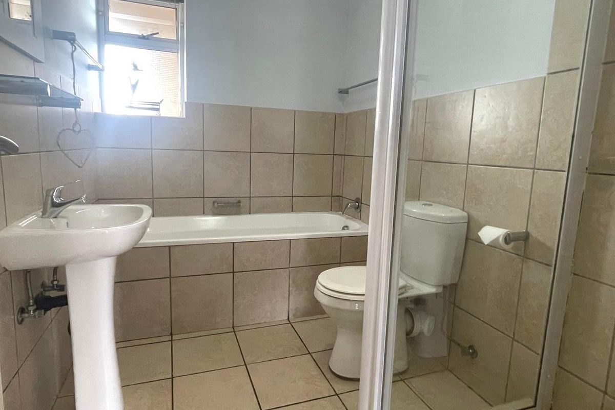 A functional bathroom featuring a pedestal basin, bathtub, and toilet with neutral wall and floor tiling.