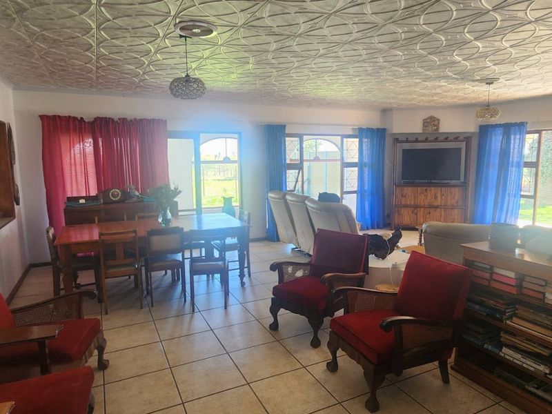 Spacious open-plan living and dining area featuring tiled flooring, large windows for natural light, and a distinctive decorative pressed metal ceiling.