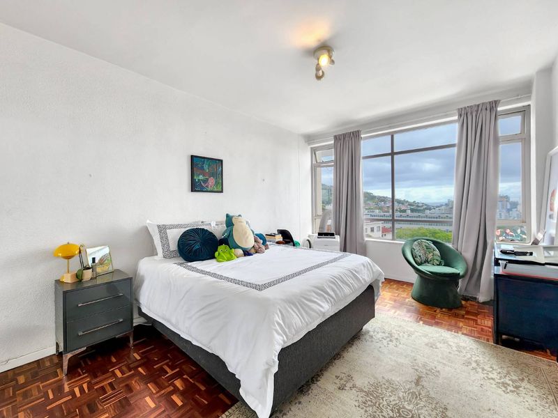A bright bedroom featuring classic parquet flooring and large windows that provide ample natural light and expansive city views.