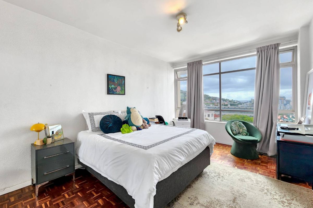 A bright bedroom featuring classic parquet flooring and large windows that provide ample natural light and expansive city views.