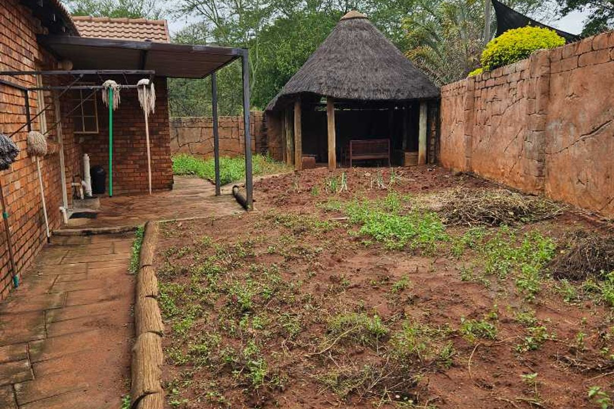 Rear garden area featuring a paved patio, a thatched lapa structure, and a perimeter boundary wall.