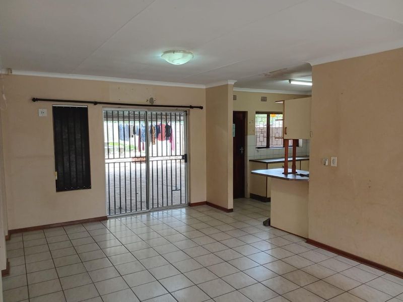 Open plan living area featuring tiled flooring, a breakfast bar, and a sliding door with security gate leading to the exterior.