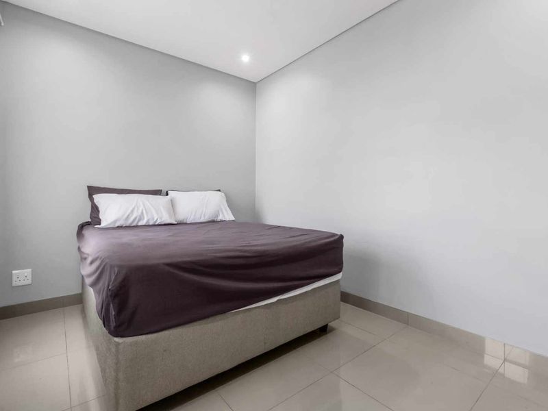 A clean and simple bedroom featuring neutral wall tones, tiled flooring, and recessed lighting, providing a blank canvas for personalization.
