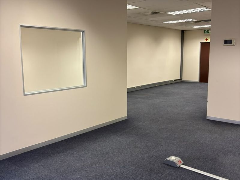 A spacious, empty office area featuring neutral walls, carpeted flooring, suspended ceilings with recessed lighting, and integrated floor-mounted power points.