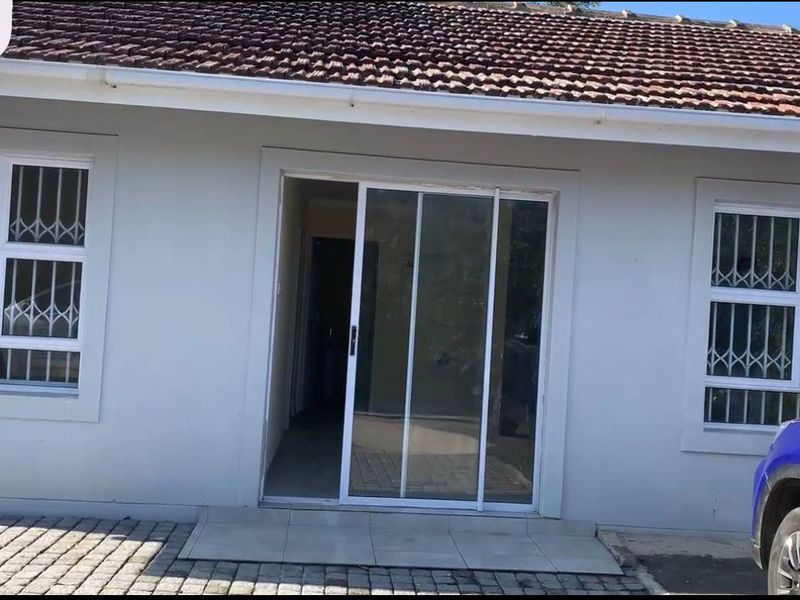 Front elevation of a cottage featuring a tiled roof, sliding glass entrance door, and windows fitted with security bars.