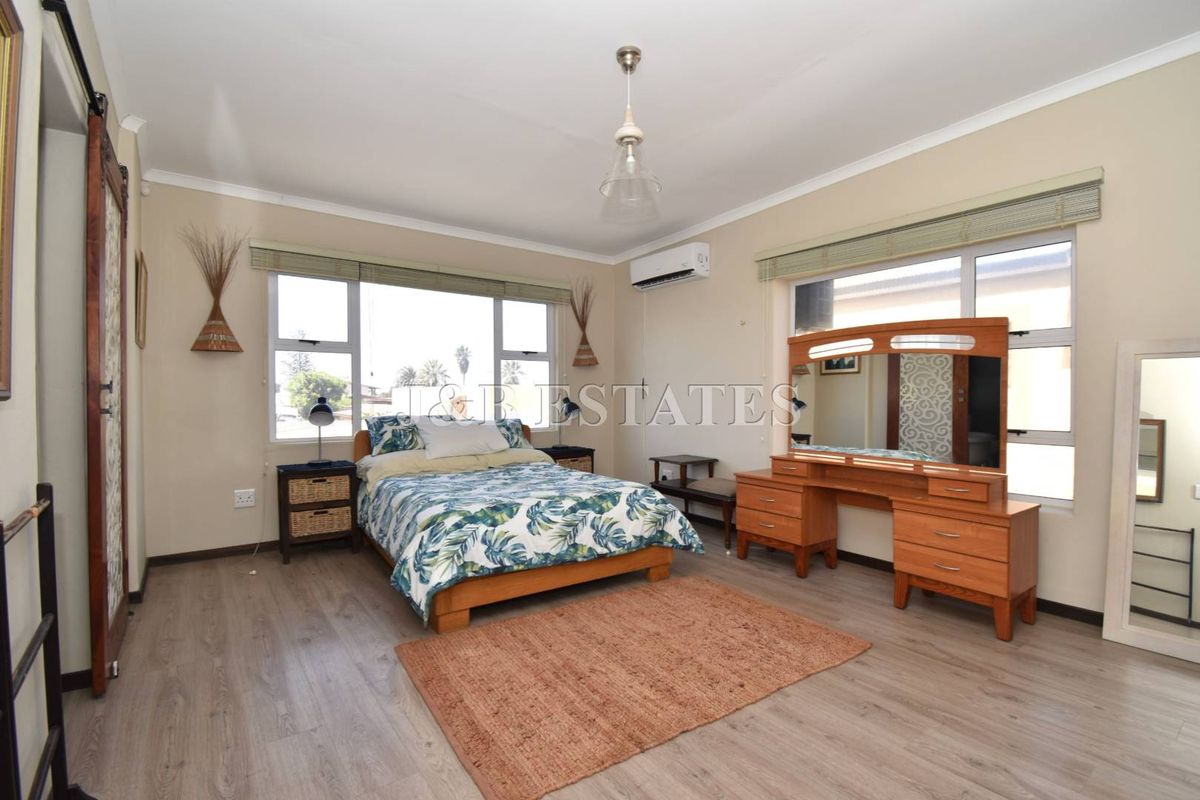 Spacious bedroom featuring light wood-look flooring, large windows for natural light, a wall-mounted air conditioning unit, and a sliding barn-style door.