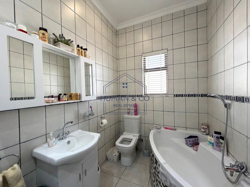 A functional bathroom featuring a corner bathtub, vanity cabinet with basin, toilet, and full-height wall tiling.