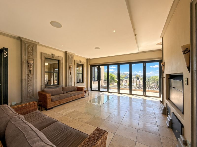 Spacious living room featuring travertine flooring, decorative stone wall detailing, a built-in fireplace, and large bi-fold doors opening to a balcony with scenic views.