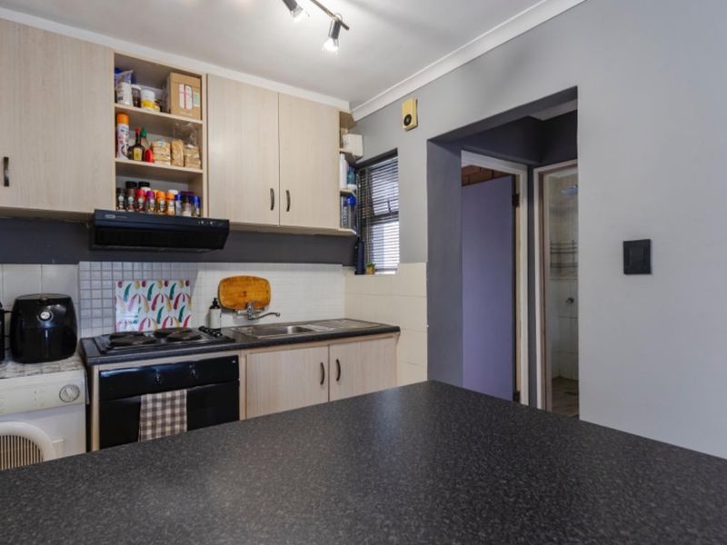 Compact kitchen featuring light wood-tone cabinetry, dark laminate countertops, built-in oven with extractor fan, and tiled backsplash, with direct access to adjacent rooms.
