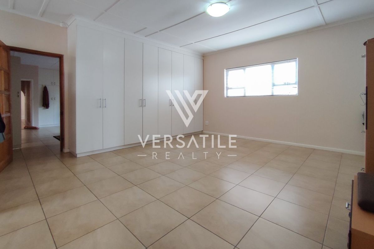 A spacious bedroom featuring neutral floor tiles, built-in cupboards, and a ceiling-mounted light fixture.