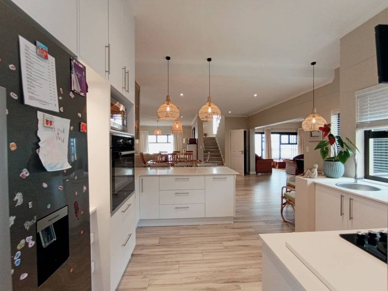 Spacious open-plan kitchen and living area featuring modern white cabinetry, integrated appliances, a central island, and light wood-look flooring throughout.