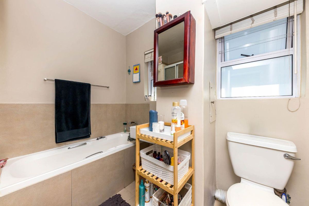 A functional bathroom featuring a built-in bathtub, toilet, and wall-mounted mirror with neutral wall tones and tiled splashback areas.