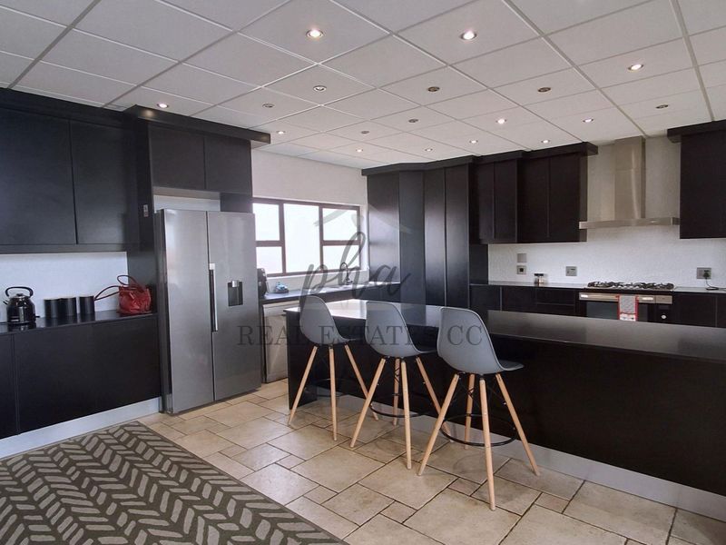 Modern kitchen featuring dark cabinetry, a central island with breakfast bar seating, built-in oven, gas hob, and tiled flooring.
