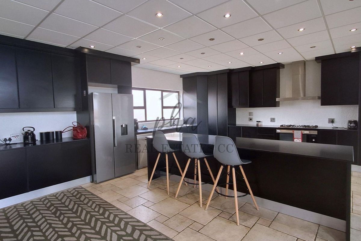 Modern kitchen featuring dark cabinetry, a central island with breakfast bar seating, built-in oven, gas hob, and tiled flooring.
