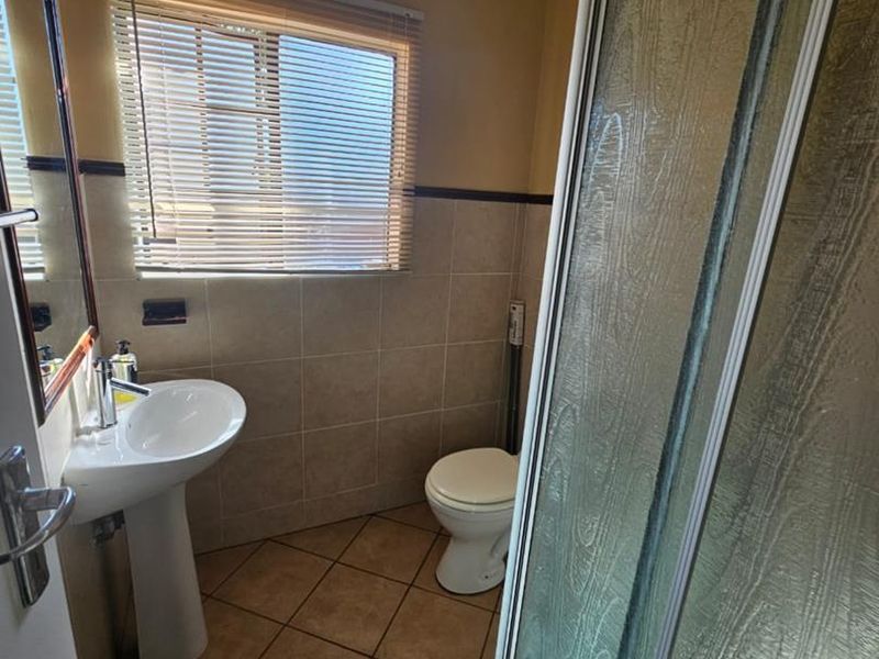 A functional bathroom featuring a pedestal basin, toilet, and a glass-enclosed shower with tiled walls and flooring.