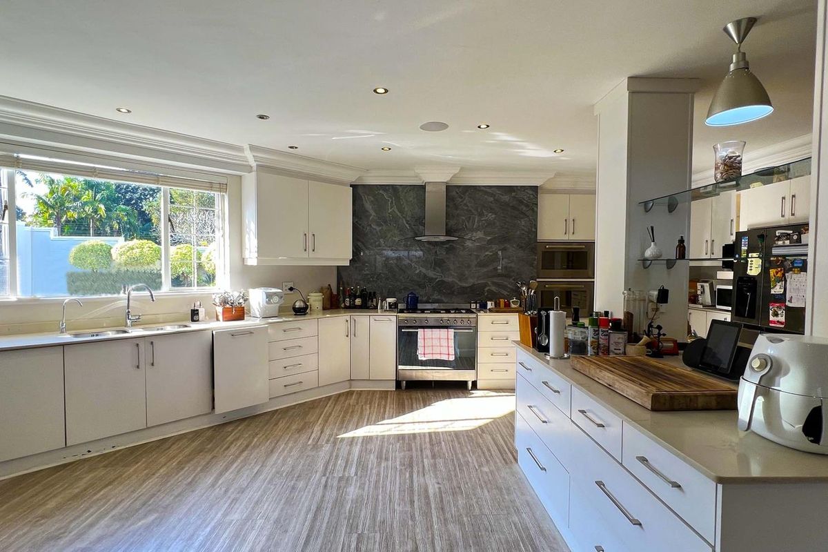 A well-appointed kitchen featuring modern white cabinetry, stone countertops, a striking stone splashback, and high-quality stainless steel appliances.