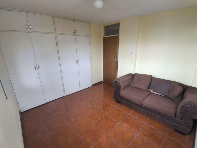 A bedroom featuring built-in cupboards, tiled flooring, and a wooden door, offering a functional space with potential for cosmetic updates.