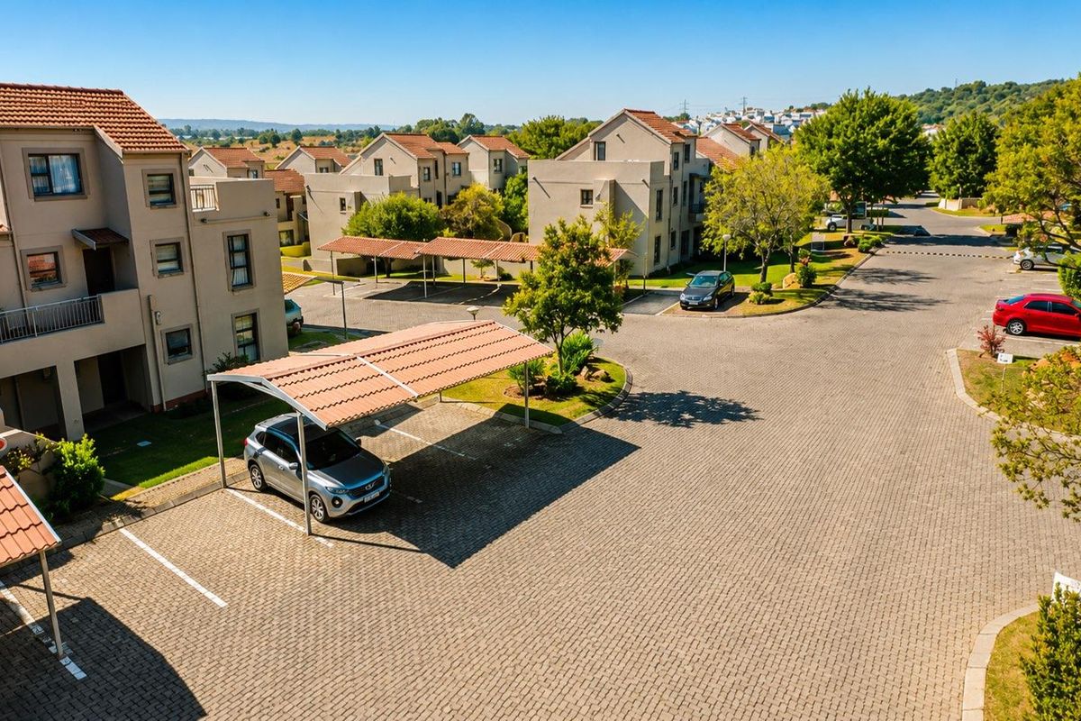 Aerial view of a townhouse complex featuring paved driveways, covered parking bays, and well-maintained communal garden areas.