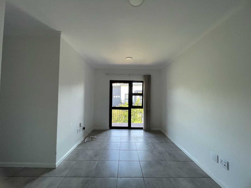 A bright, empty living area featuring neutral tiled flooring and a large sliding glass door providing access to an outdoor space.