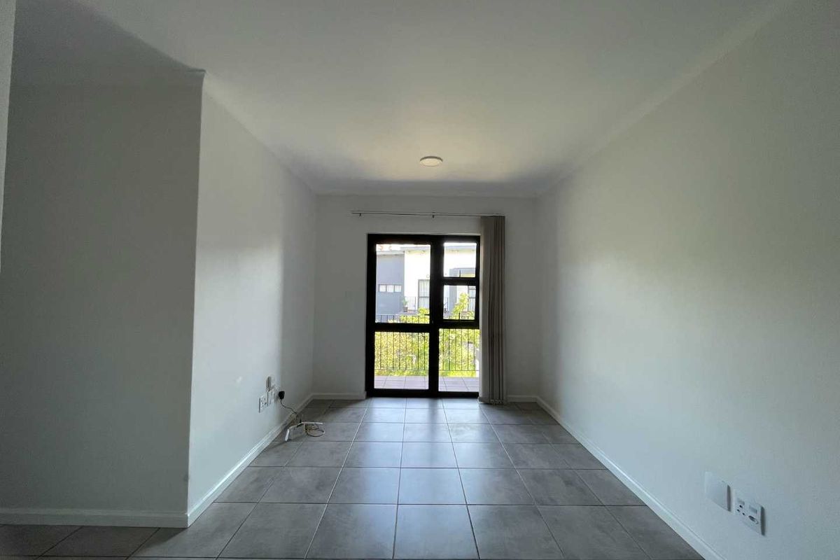 A bright, empty living area featuring neutral tiled flooring and a large sliding glass door providing access to an outdoor space.